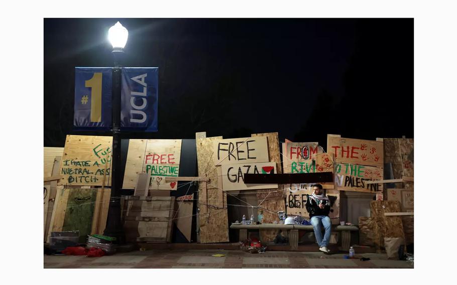 A protester at UCLA sits in front of an encampment’s particle-board wall after an order to disperse was given by law enforcement early Thursday morning. 