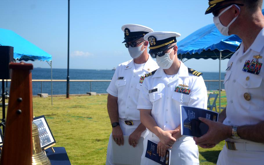 Leaders at Yokosuka Naval Base, Japan, including installation commander Capt. Rich Jarrett, right, look at photos of fallen sailors during a Bells Across America service, Thursday, Sept. 23, 2021. 