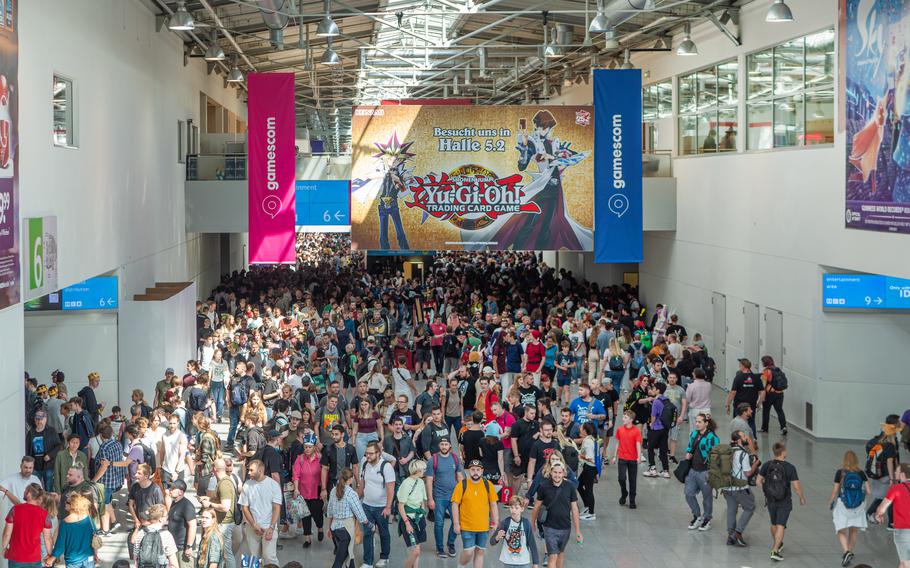 Large crowds of people enter an exhibition hall with a large colorful banner hanging over the entryway.