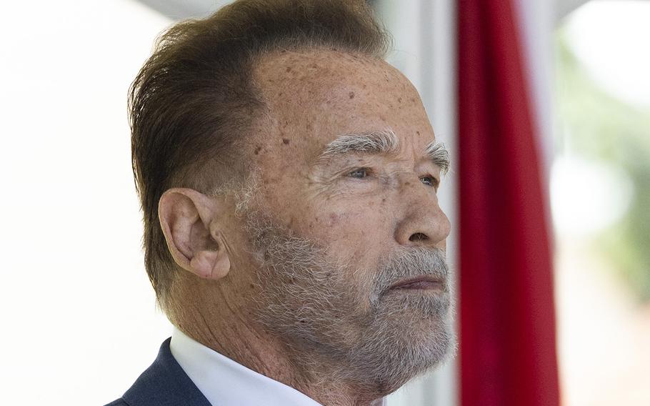 Arnold Schwarzenegger standing and placing his hand over his heart during a rendition of the national anthem.
