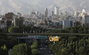 A city skyline is seen from a distance with a bridge over a highway in the foreground.