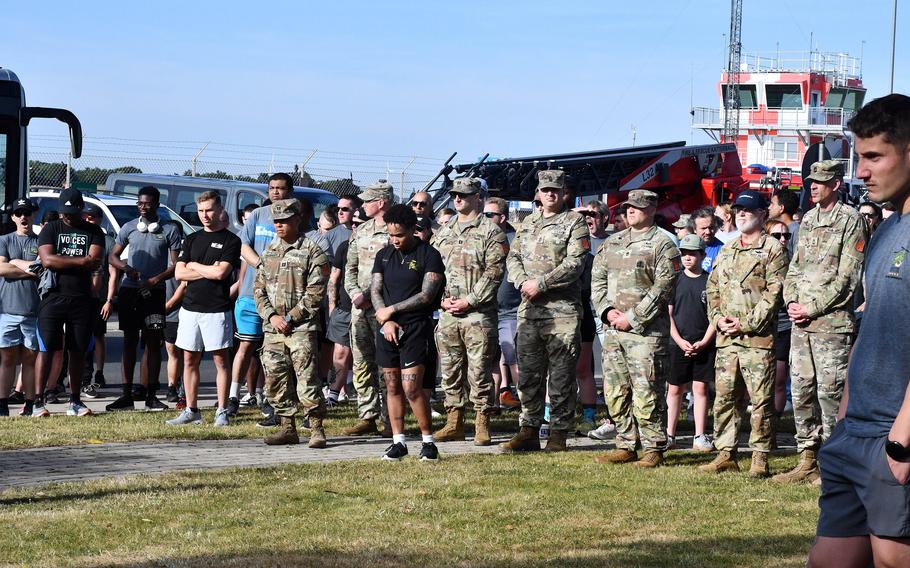 Soldiers stand in a line with their hands clasped in front of them.