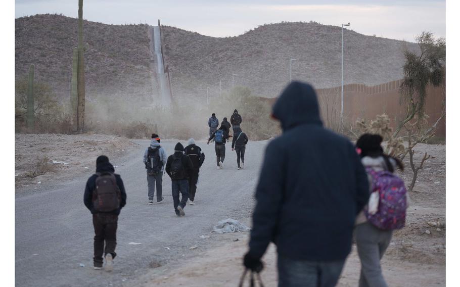 Migrants walk along the border fence at the US-Mexico border in Lukeville, Arizona.