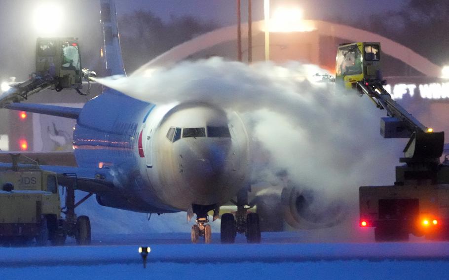 An American Airlines plane is de-iced as high winds whip around 7.5 inches of new snow at Minneapolis-St. Paul International Airport Thursday, Dec. 22, 2022. 