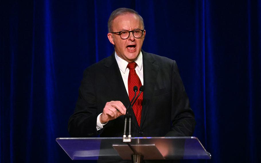A man in a suit and red tie speaks vigorously at a podium.