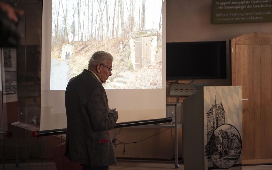 An elderly man stands in front of a projector screen