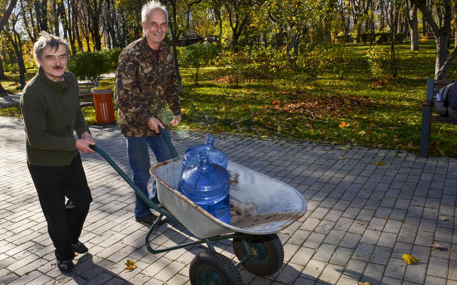 Nikolai Token, right, and his compatriot push a wheelbarrow filled with two water jugs through Taras Shevchenko Park in Kyiv, Ukraine, on Oct. 31, 2022. Token and his friend said they regularly stock up on water from the park due to water outages. 