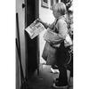 A boy stands in front of a door carrying newspapers.
