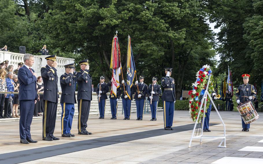 Army leaders and others stand at attention, some saluting, others with their  right hand over their heart during a ceremony.