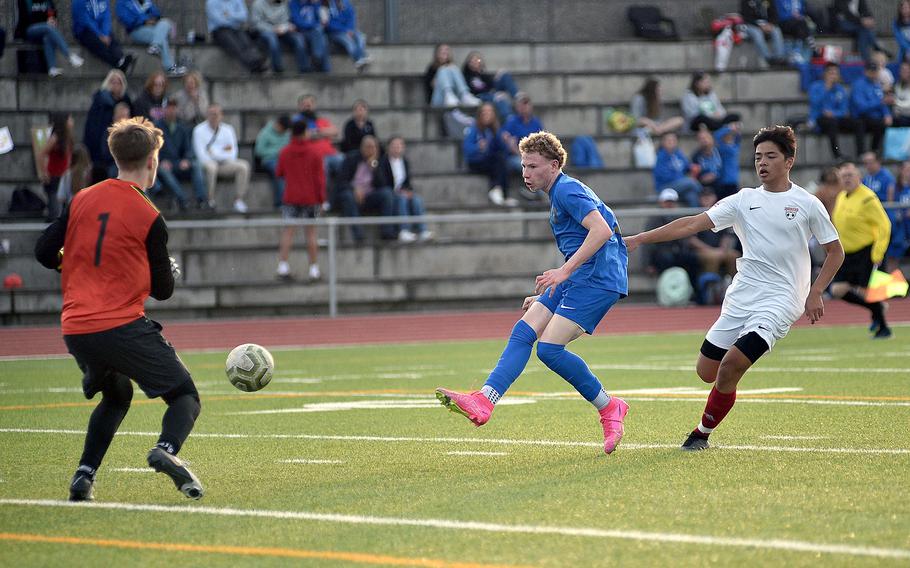 Ramstein striker Joseph Yost shoots past Kaiserslautern goalkeper Phoenix Meikle to score during a match on April 12, 2024, at Ramstein High School on Ramstein Air Base, Germany. Trailing the play is Raider defender Gavin Cahanding.
