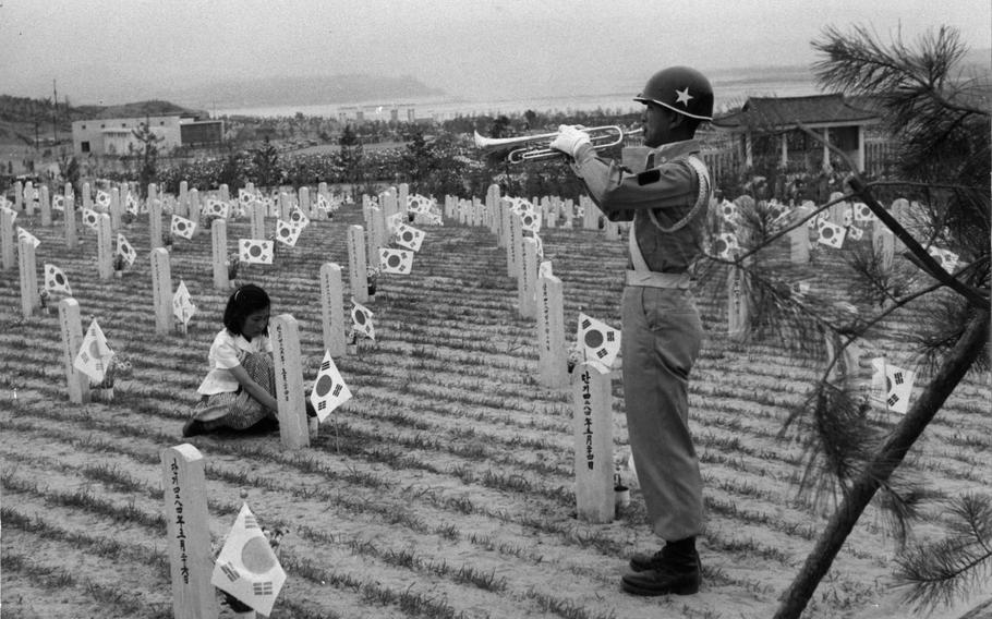 A bugler sounds a call for the dead while a girl arranges flowers at a soldier’s grave.