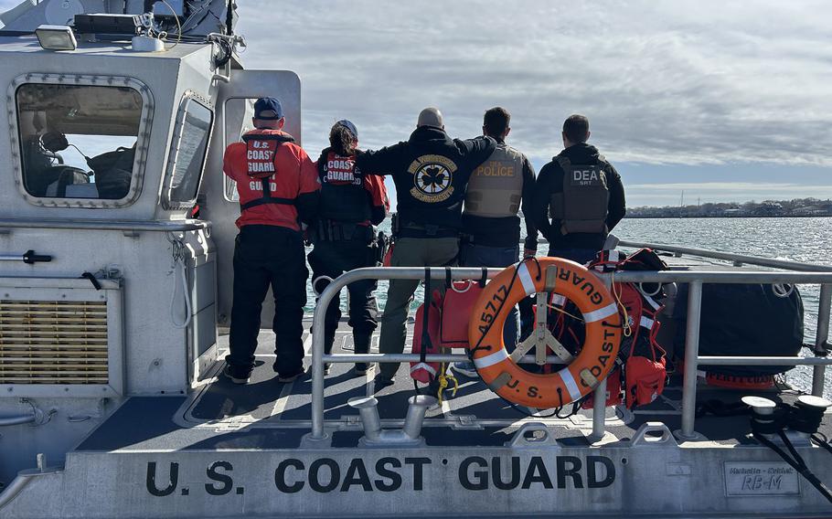 Members of the U.S. Coast Guard members seen from behind standing at a boat with undocumented immigrants they arrested.