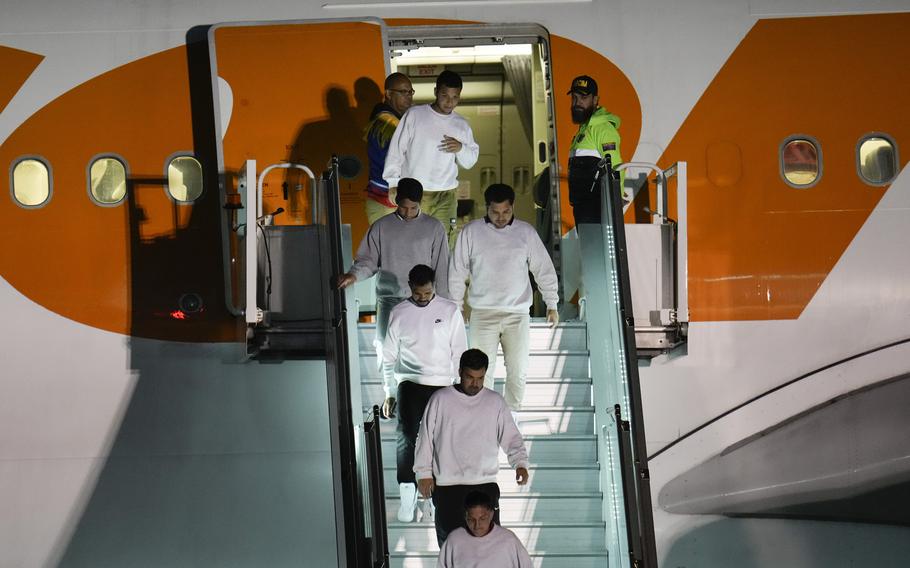 Migrants in white or gray sweatshirts walk down a plane staircase.