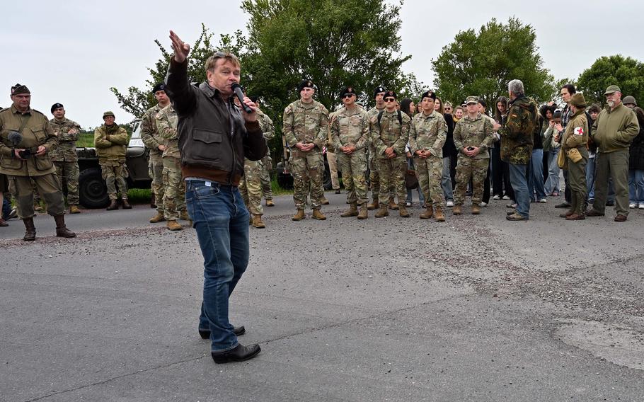 Uniformed soldiers and World War II reenactors listen to a man speak.