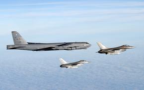 An American B-52H Stratofortress flies in a blue sky alongside two Danish air force F-16s.