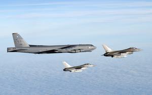 An American B-52H Stratofortress flies in a blue sky alongside two Danish air force F-16s.