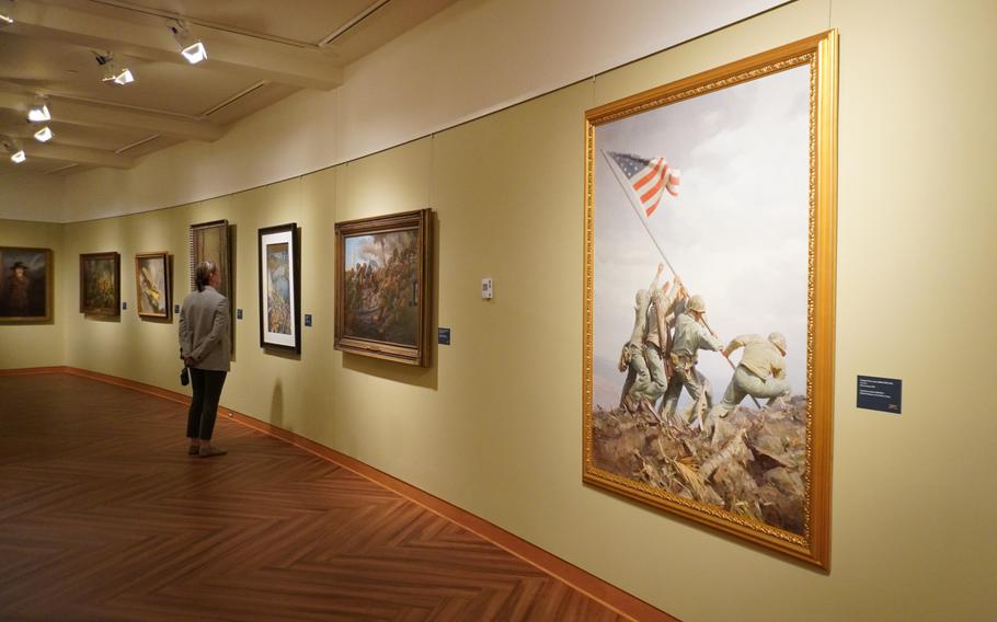 A woman looks at paintings on a wall.