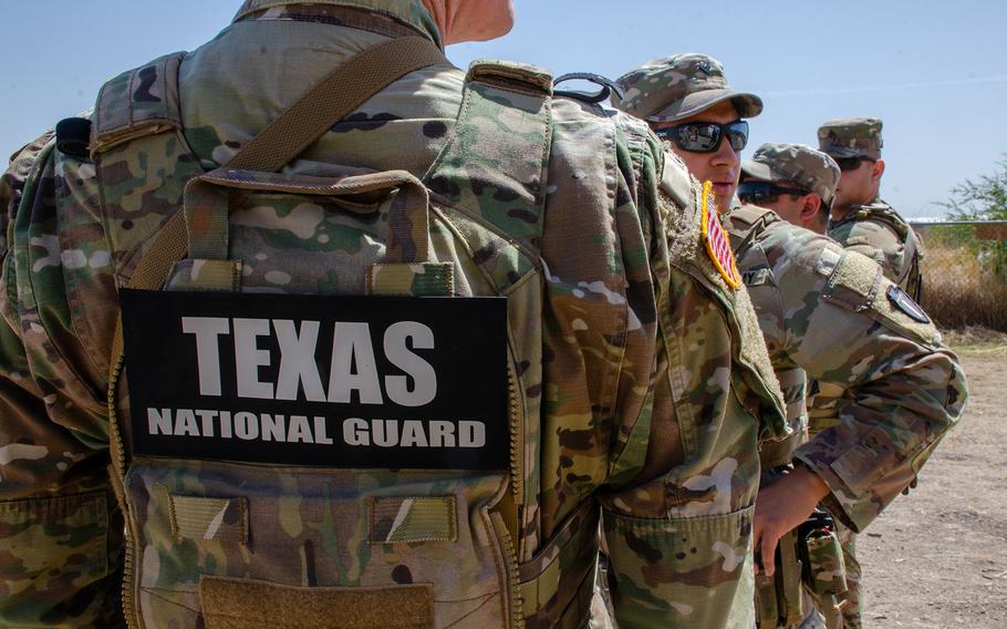 Troops standing around with one soldier wearing a label on his back that reads, “Texas National Guard.”