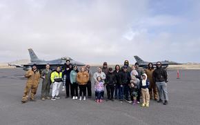 Airmen and civilians take a picture in front of F-16 aircraft.