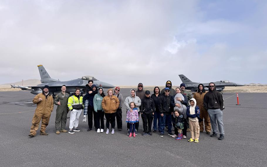 Airmen and civilians take a picture in front of F-16 aircraft.