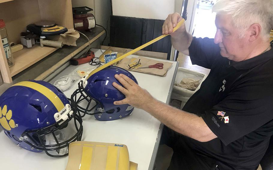 Yokota coach Tim Pujol applies Panther paw and yellow-striped decals to his team helmets.