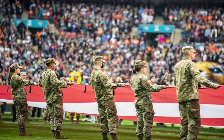 Airmen from the 501st Combat Support Wing unveil a giant American flag during the national anthem, before an NFL game at Wembley Stadium, in London, England, Oct. 30, 2022. A new memo from the Defense Department public affairs office is prohibiting the use by uniformed service members of giant U.S. flags during sporting events and parachute jumps.