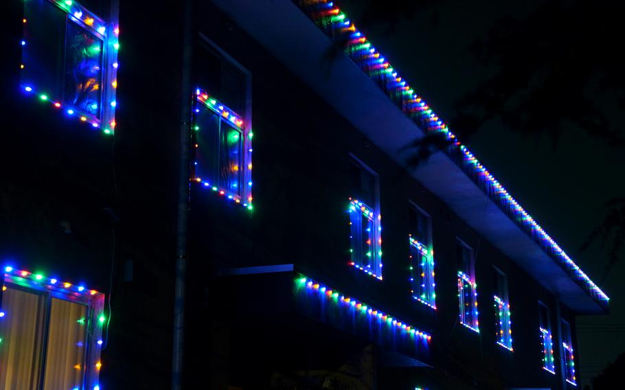 A house illuminated at night with strings of multi-colored Christmas lights around the windows and along the roof.