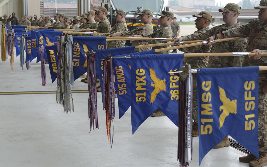 Several soldiers sand in a line and hold blue flags with yellow lettering representing their units, during a change-of-command ceremony at Osan Air Base, South Korea, June 27, 2025.