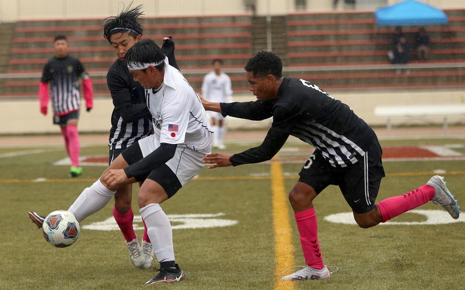 Zama's Kaisei Muta tries to keep the ball from Matthew C. Perry's Nemo Hines and Edward Pacleb during Tuesday's rainy Division II boys soccer match. The Trojans won 2-0.