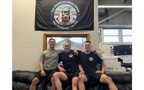 U.S. Coast Guard Petty Officer 2nd Class Nicholas Mauricio, Petty Officer 2nd Class James Lowen and Petty Officer 3rd Class Bradley Beauchamp, each an aviation survival technician at Air Station Traverse City, pose for a picture in the rescue swimmer shop at the air station in Traverse City, Michigan, July 31, 2025. Prior to the photo, the swimmers rescued a person from an explosion at an establishment nearby the air station. (Coast Guard courtesy photo by Air Station Traverse City)