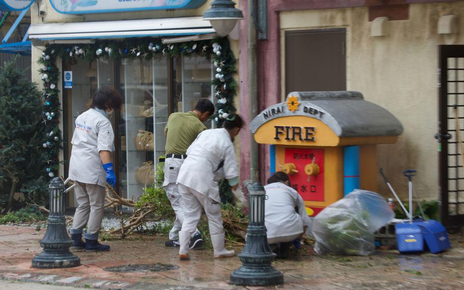 Japanese workers clean up debris from a tree toppled by Typhoon Khanun at American Village in Chatan, Okinawa, Thursday, Aug. 3, 2023. 