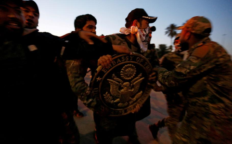 Protesters and militia fighters carry the logo of the U.S. Embassy during a protest to condemn air strikes on bases belonging to Hashd al-Shaabi (paramilitary forces), in Baghdad, Dec. 31, 2019.