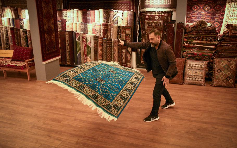 Vedat Tan twirls an Afghan rug, colored blue with indigo dye, at his shop in an area known as "American Alley" outside the gate of Incirlik Air Base in southern Turkey on Feb. 27, 2023. Tan said recent earthquakes forced him to live in his car for almost two weeks, and that neighbors died in the disaster. 