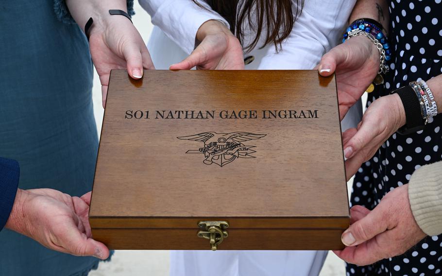 The hands of four people hold a wooden box for Nathan Gage.