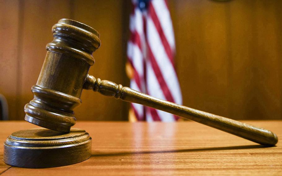 A wooden gavel rests on a small pedastal on a courtroom bench in front of a U.S. flag.