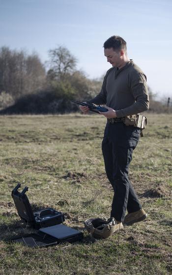 A soldier tests a homemade drone in a field.