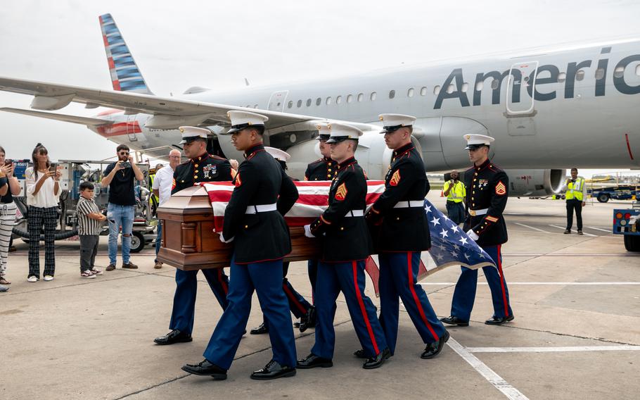 Marines carry a casket on the runway of an airport.