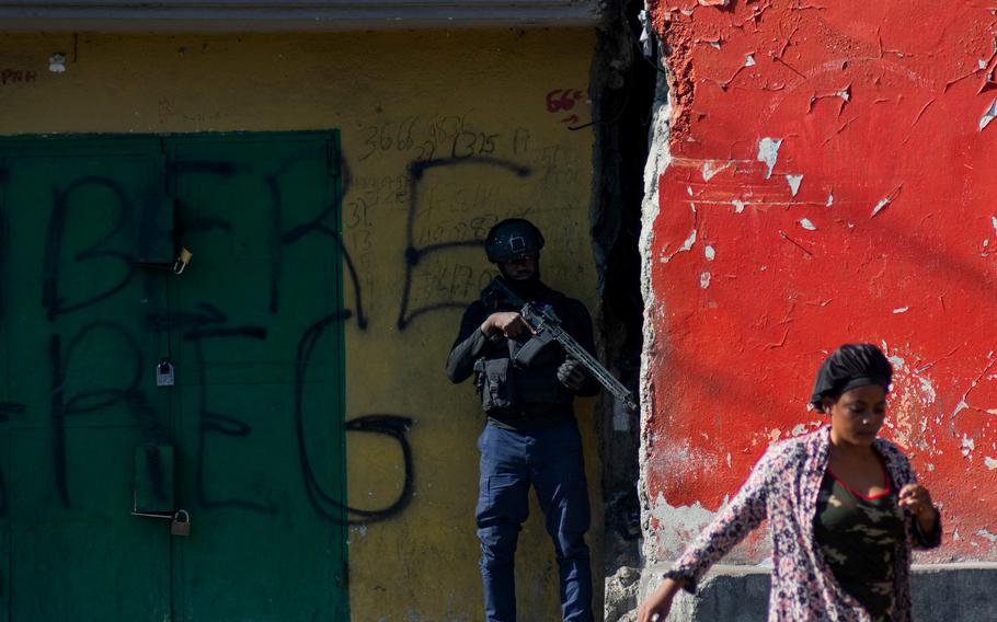 A woman walks past an armed police officer monitoring a street after gang violence the previous night, on March 22, 2024, in Port-au-Prince, Haiti. 
