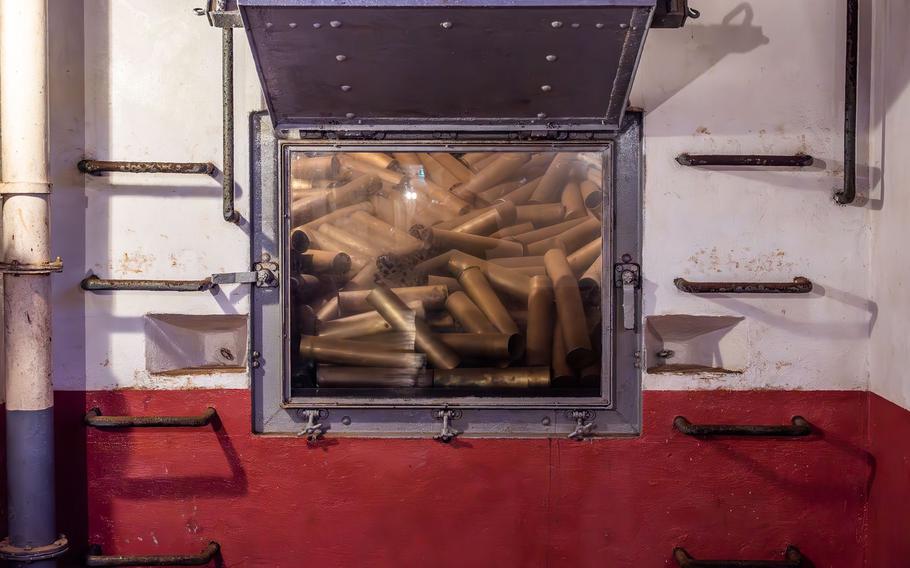 Ammunition storage compartment with glass viewing window showing numerous artillery shells or munitions stored inside a secure military facility.