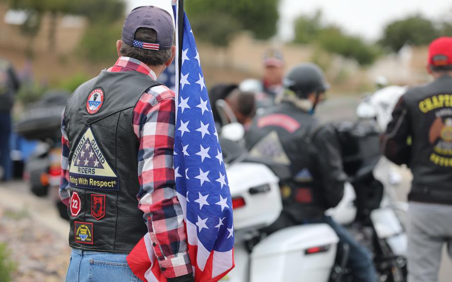 A motorcyclist stands with an American flag.