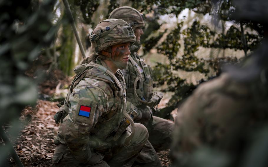 A U.K. soldier wearing camouflage and face paint sits with her squad.