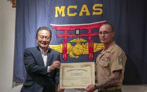A man in a suit hands a letter of appreciation to a Marine in uniform as they pose for a photo.