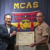 A man in a suit hands a letter of appreciation to a Marine in uniform as they pose for a photo.