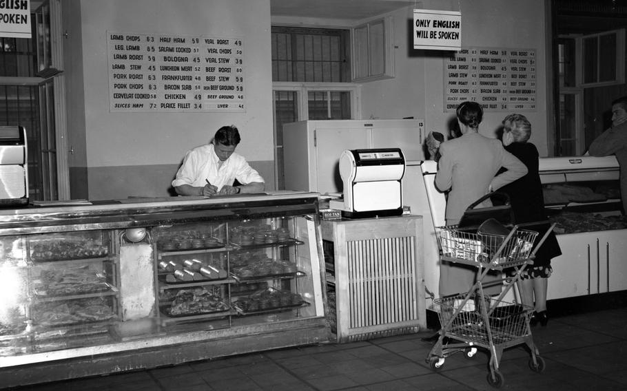 A black and white photo of a meat section at a commissary, with two women standing in front of a counter.