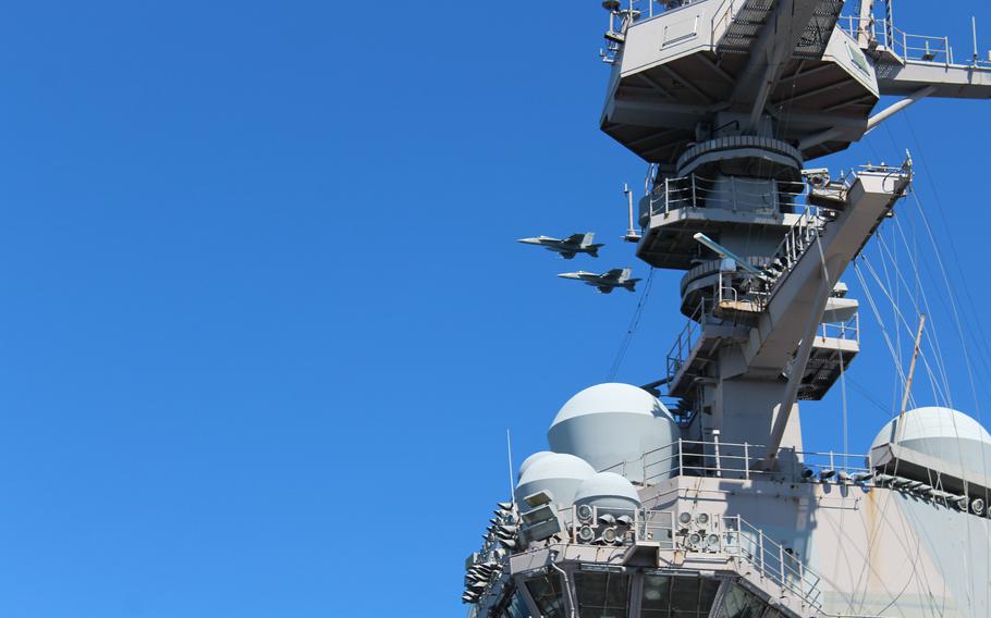 Two fighter jets fly over a ship.