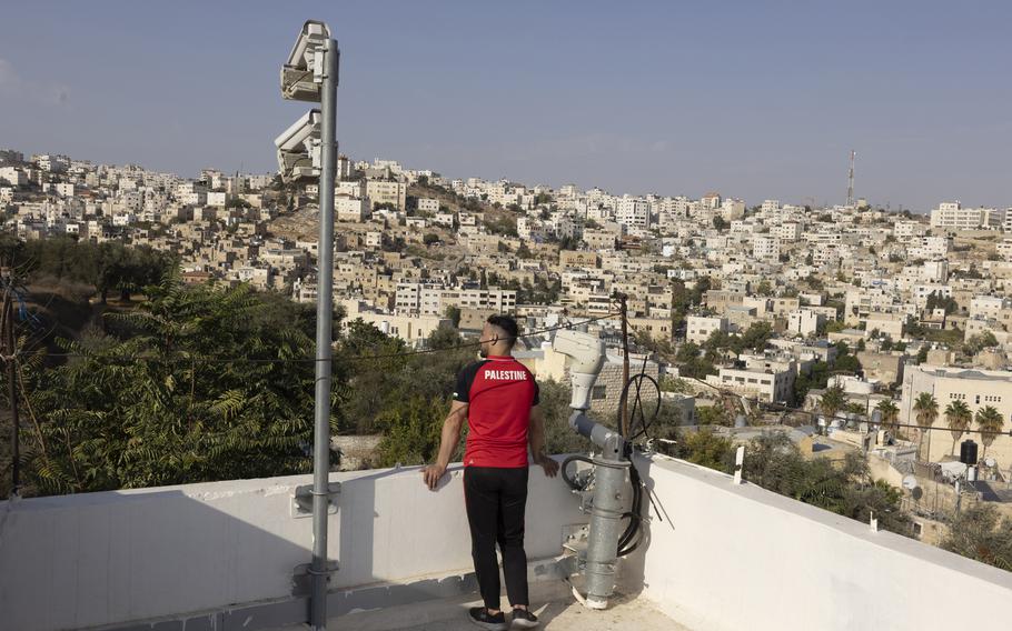 A Palestinian man stands next to surveillance cameras placed on a roof by the Israeli army the West Bank city of Hebron on Oct. 13, 2021. 