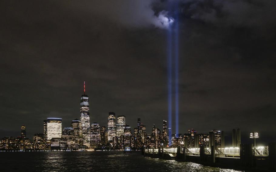 The illuminated skyline of New York is seen at night, with two vertical beams of blue light representing the twin towers of the World Trade Center.