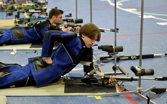 Ansbach's Alexander Pohlman reaches into his pocket while in the prone position during the DODEA European marksmanship championship Saturday at WIesbaden High School in Wiesbaden, Germany. In the background, teammate Collin Robertson takes aim.