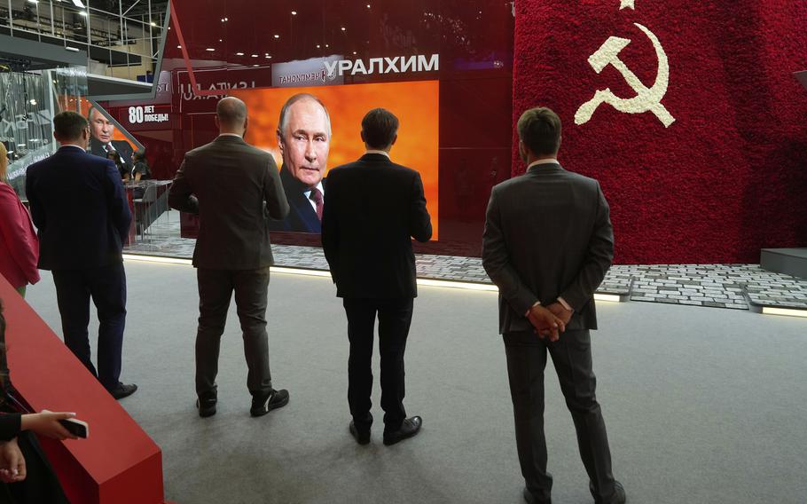 Men stand in front of a TV screen.