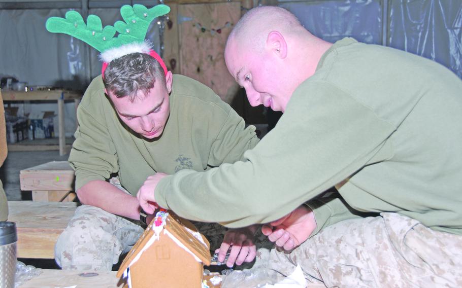 Pfc. Derik Briskey, left, 21, and Sgt. Justin Caughey, 26, reservists with Company B, 6th Engineer Support Battalion serving in Iraq with the 9th Engineer Support Battalion out of Okinawa, build a gingerbread house complete with a protective Hesco barrier surrounding the front (made from Scrabble letters spelling “Hesco”), Dec. 24, 2006. But the house didn’t make it to completion; the roof collapsed. “I guess we can eat the glue now,” Briskey, wearing reindeer ears, said, grabbing the icing. 